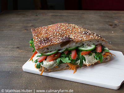 Sandwich mit frischem Fladenbrot, Hummus, Rucola, Tomaten, Gurke und Karotte